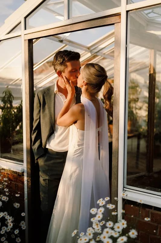 Couple kissing by a greenhouse at golden hour